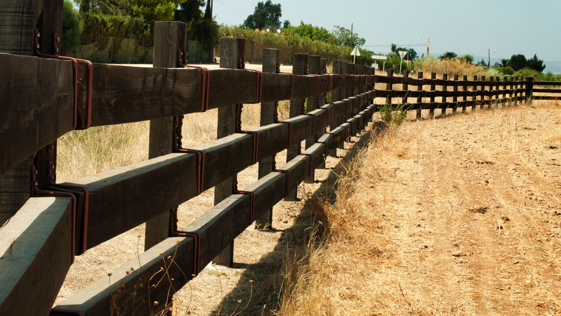 Wooden fence along dry grassland with trees and sky in background