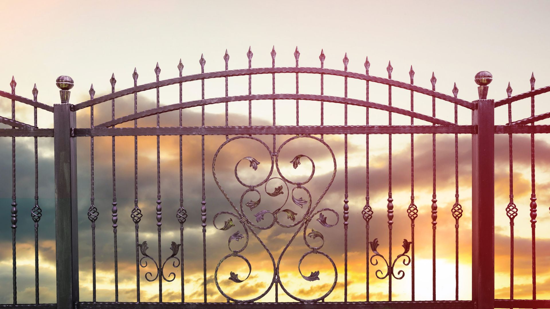 Ornate wrought iron gate with decorative scrollwork against dramatic sunset sky