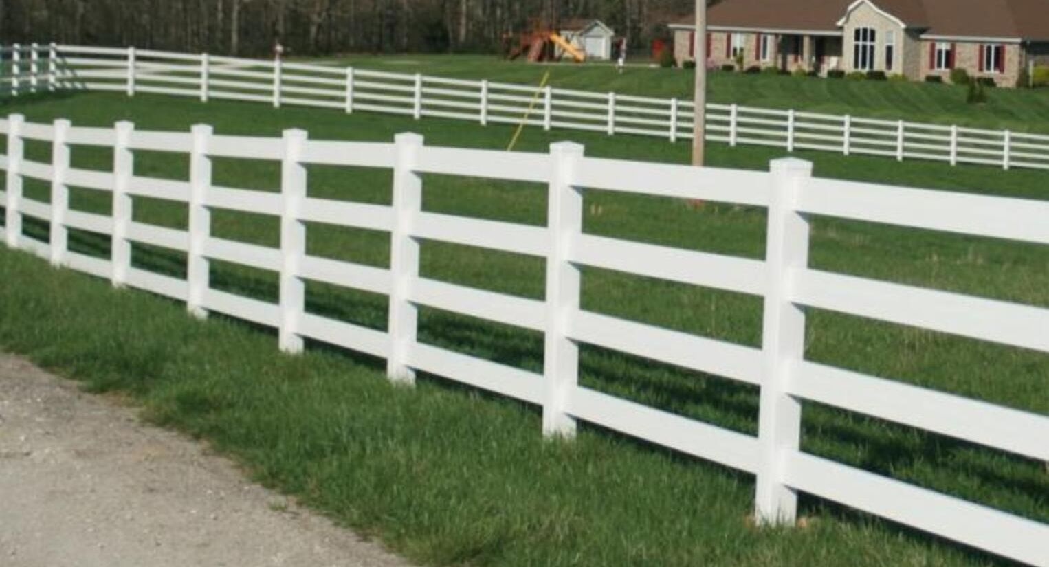 White wooden fence bordering green lawn with houses in background