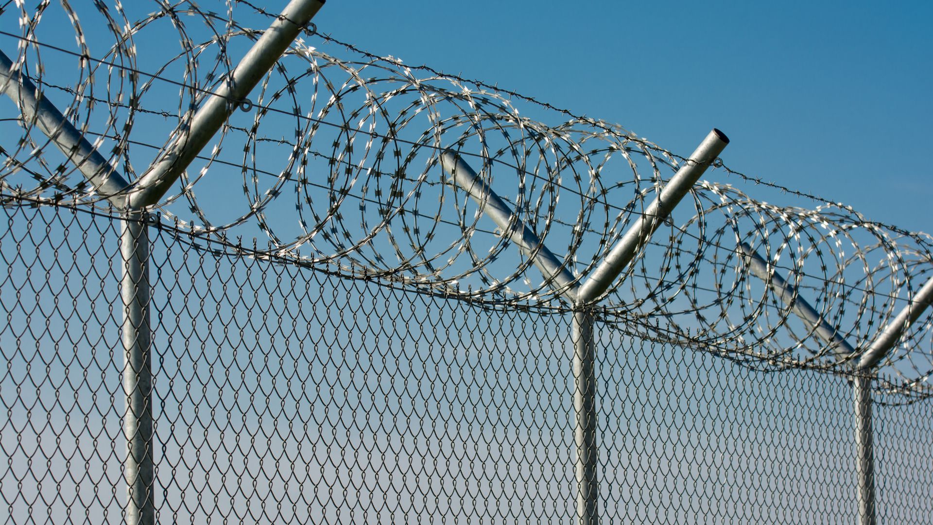 Barbed wire and chain-link fence against a clear blue sky