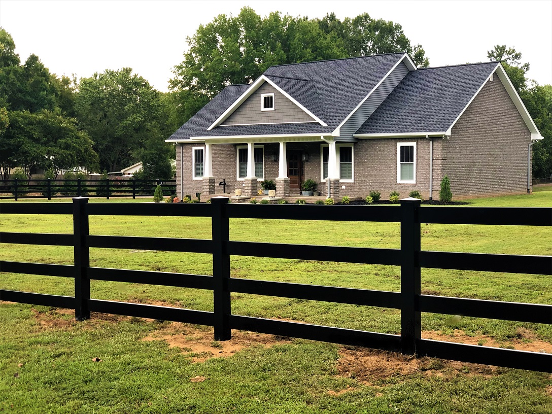 Brick house with black wooden fence on green lawn surrounded by trees