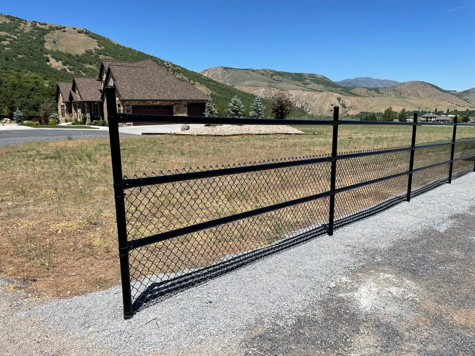 Black chain-link fence with mountain landscape and stone house in background