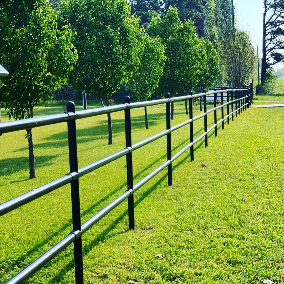 Metal railing along green grassy field with trees in background