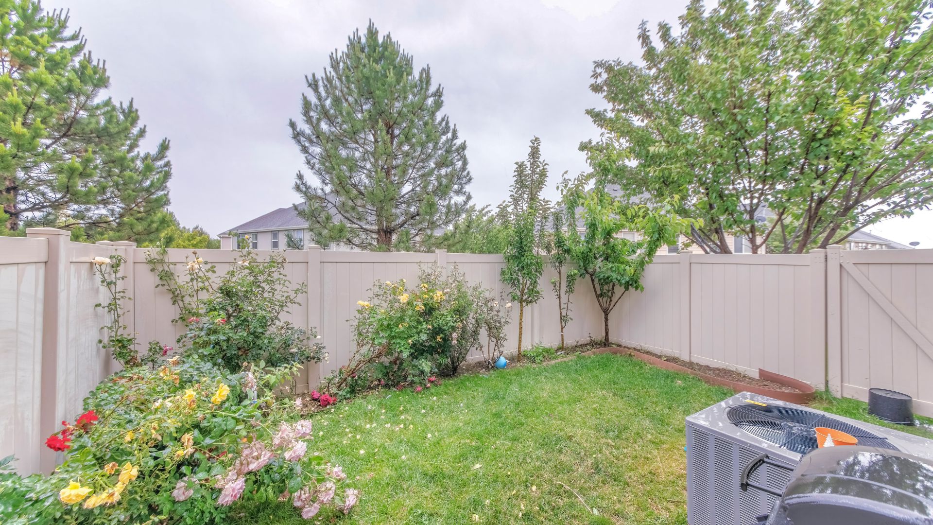 Suburban backyard with white fence, flowering plants, and green lawn