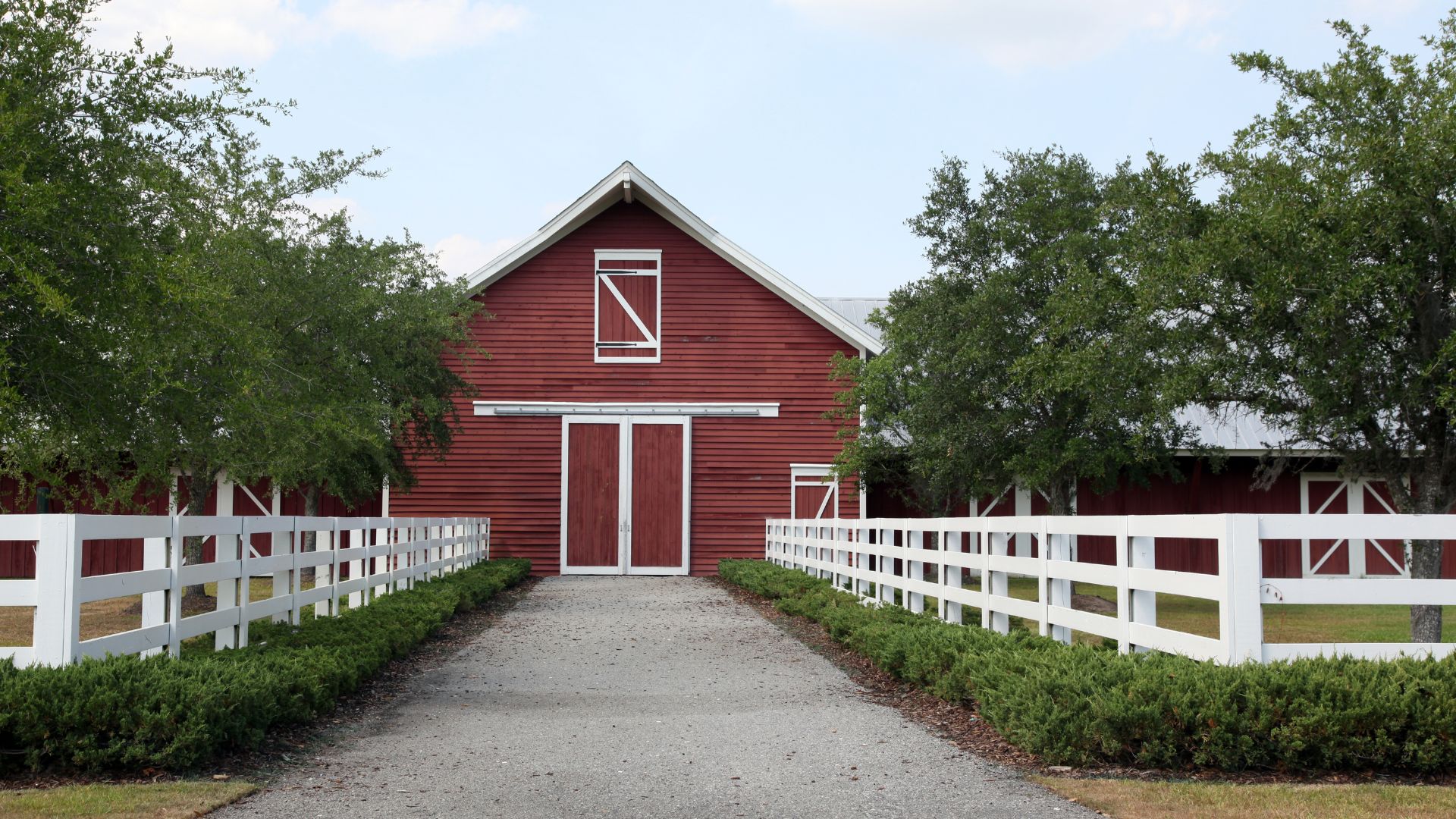 Red barn with white fence and green shrubs on a gravel path