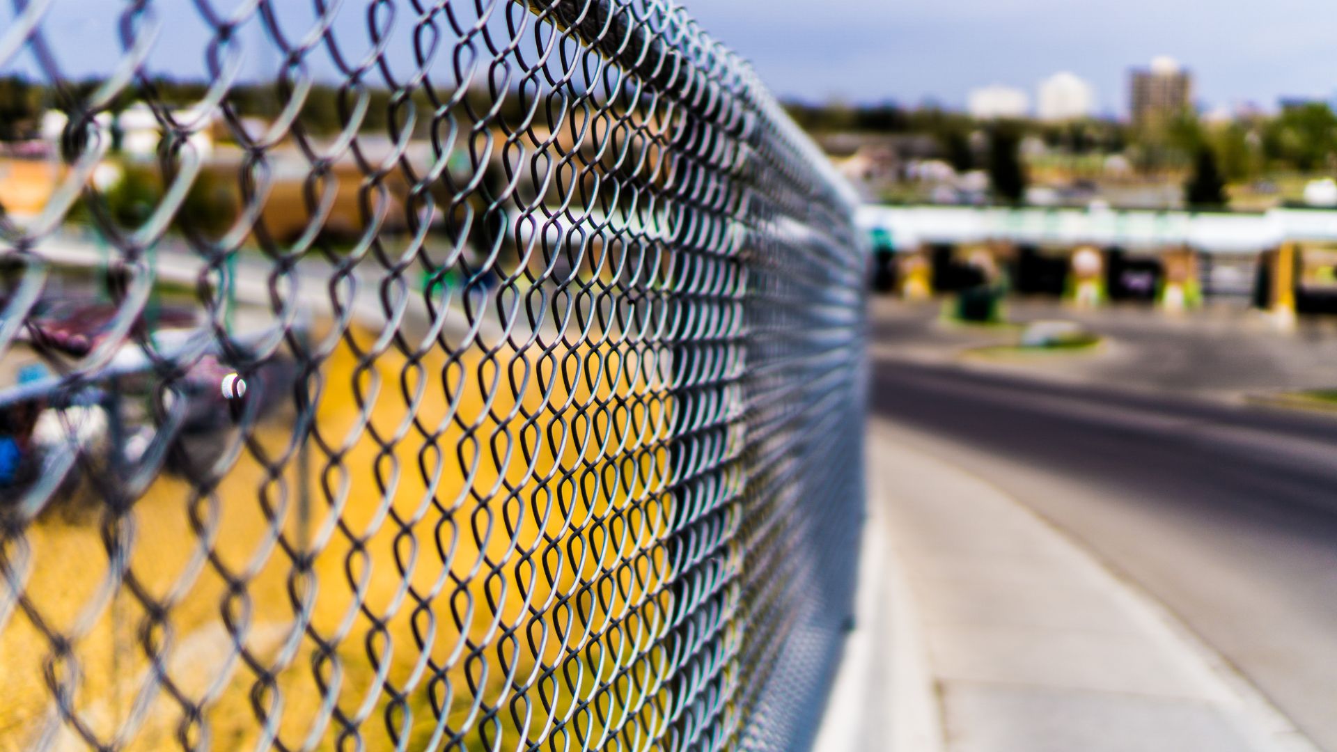 Close-up of chain-link fence with blurred urban street background