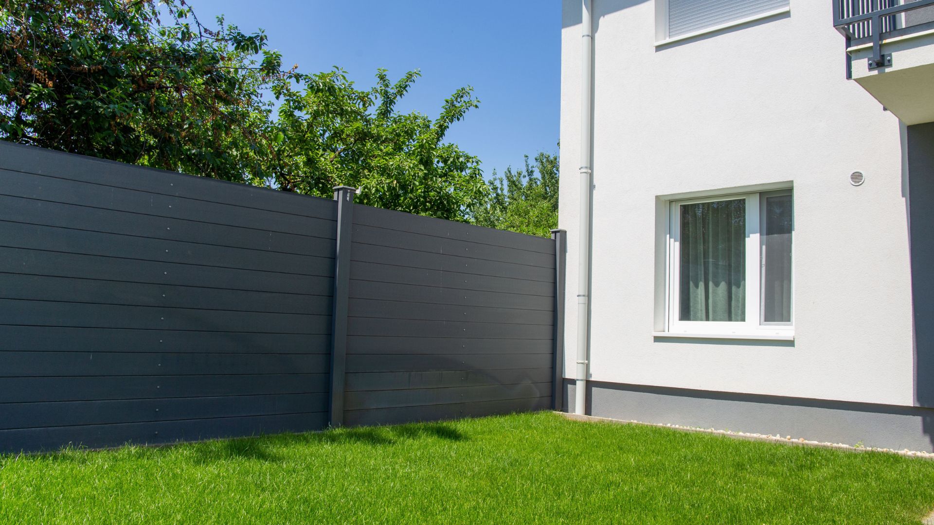 Modern white house with dark fence and trimmed green lawn