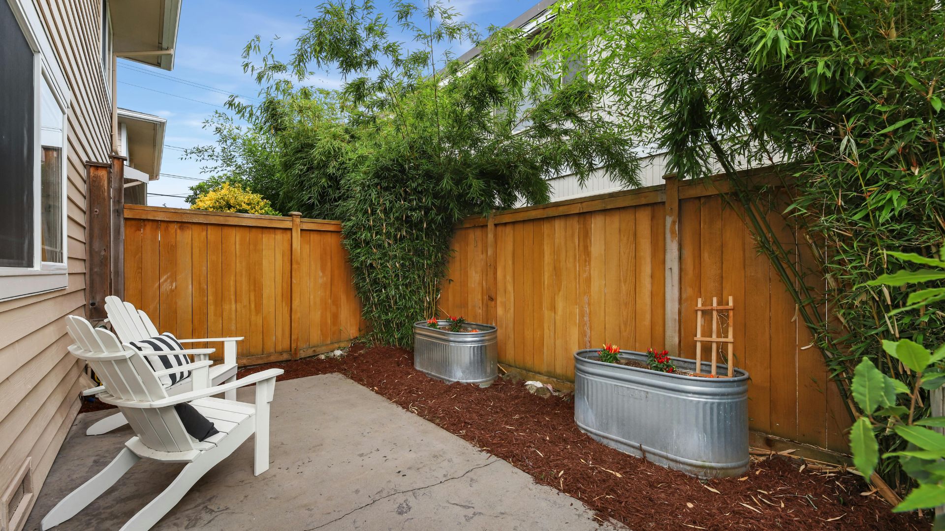 Backyard with white Adirondack chairs, metal planters, and wooden fence