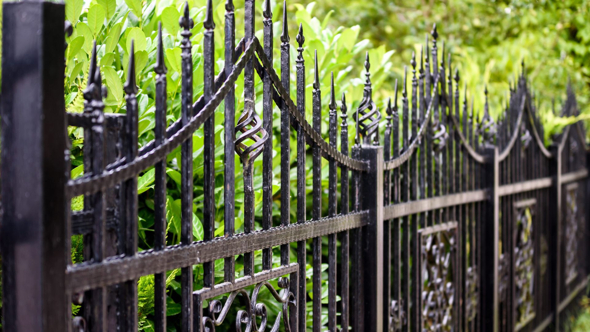 Ornate black metal fence with decorative spikes against lush green foliage