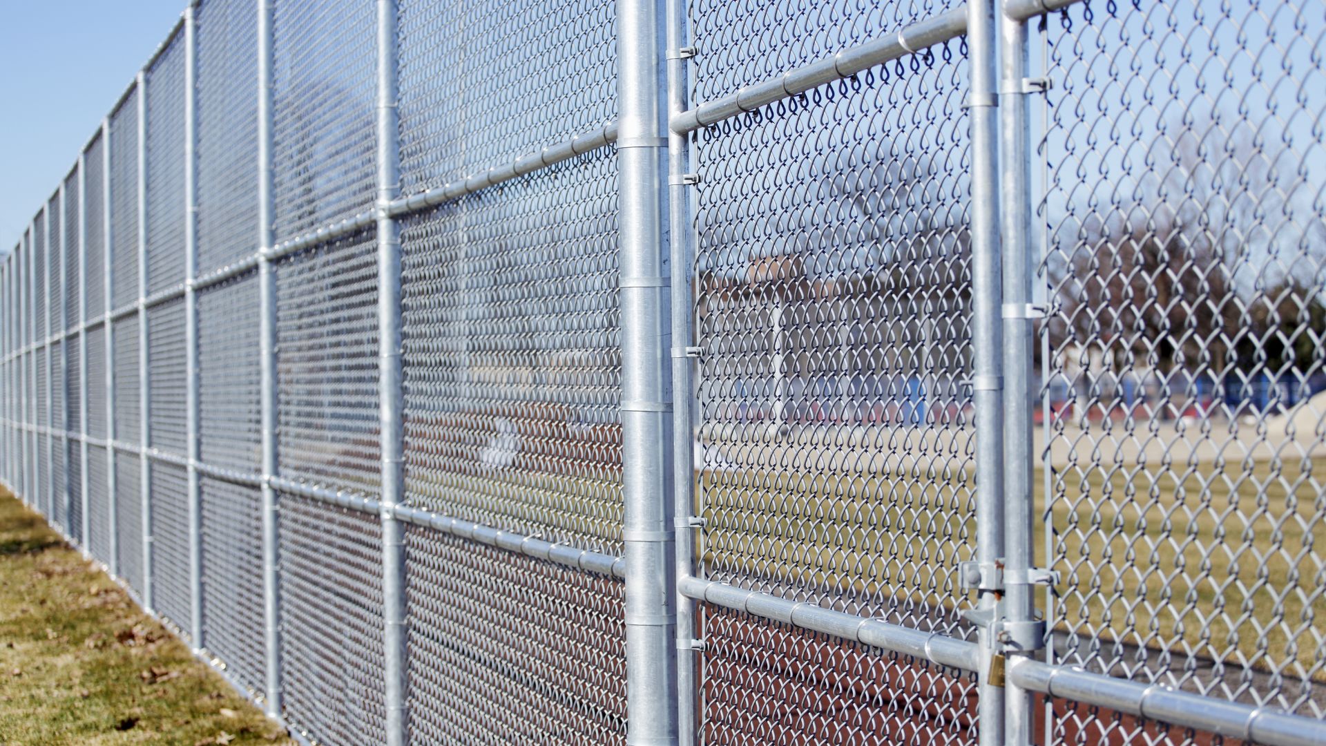 Chain-link fence with metal poles extending across grassy field
