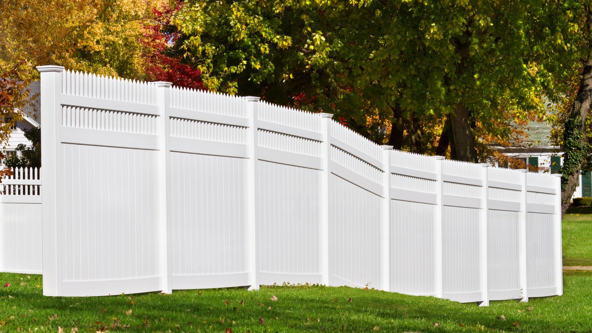 White vinyl fence on green lawn with colorful autumn trees in background