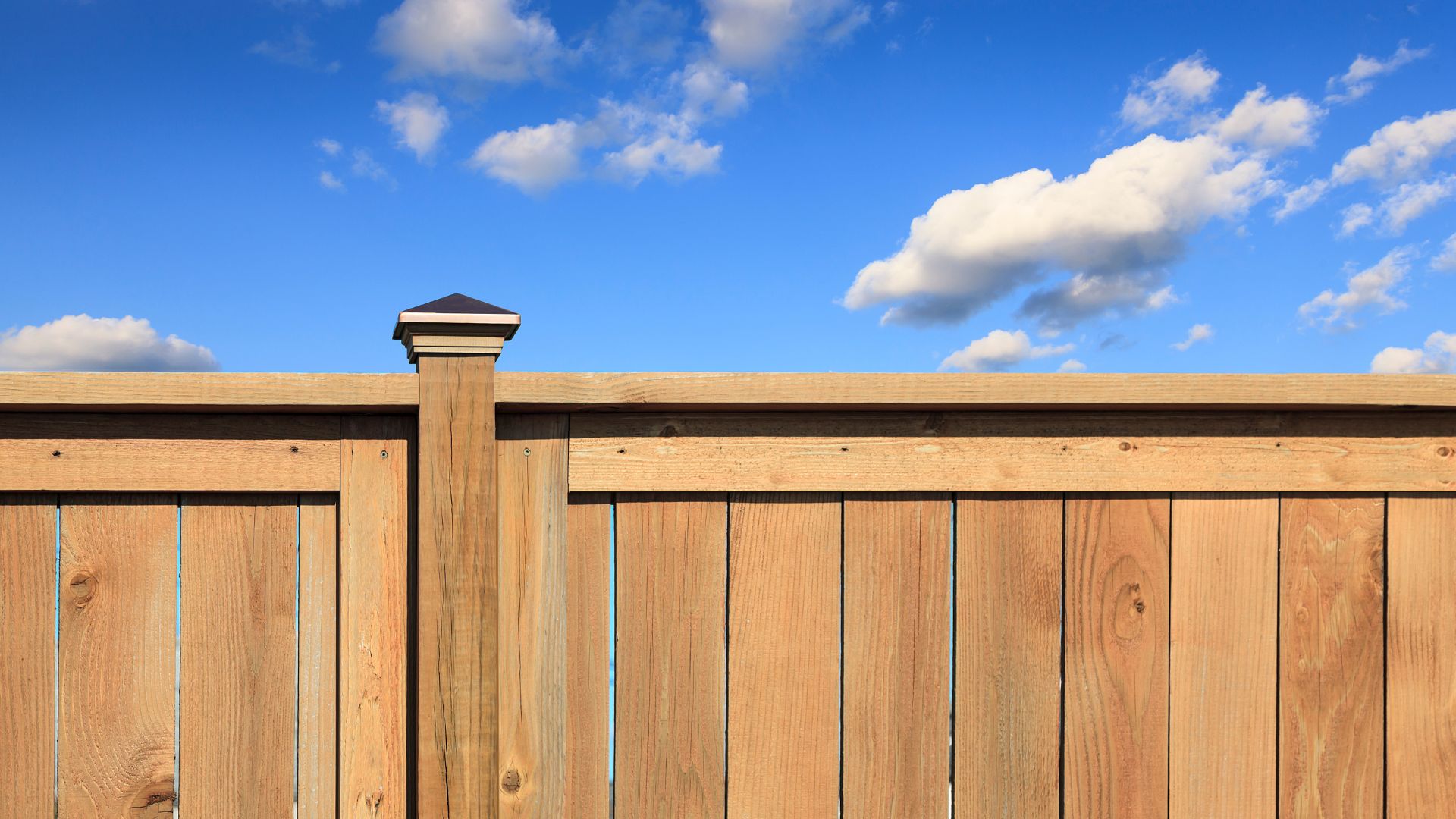 Wooden fence with wooden post against bright blue sky with fluffy clouds