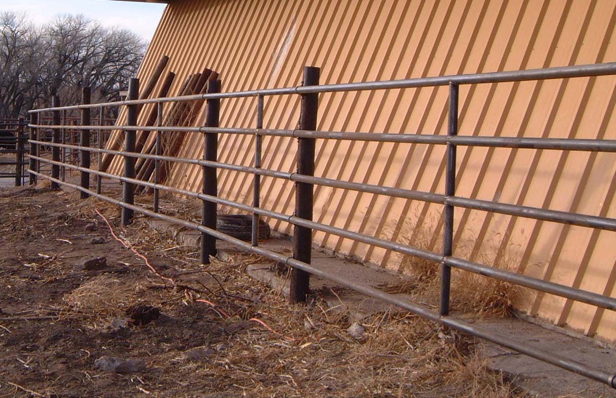 Wooden barn wall with metal fence and straw-covered ground in rural setting