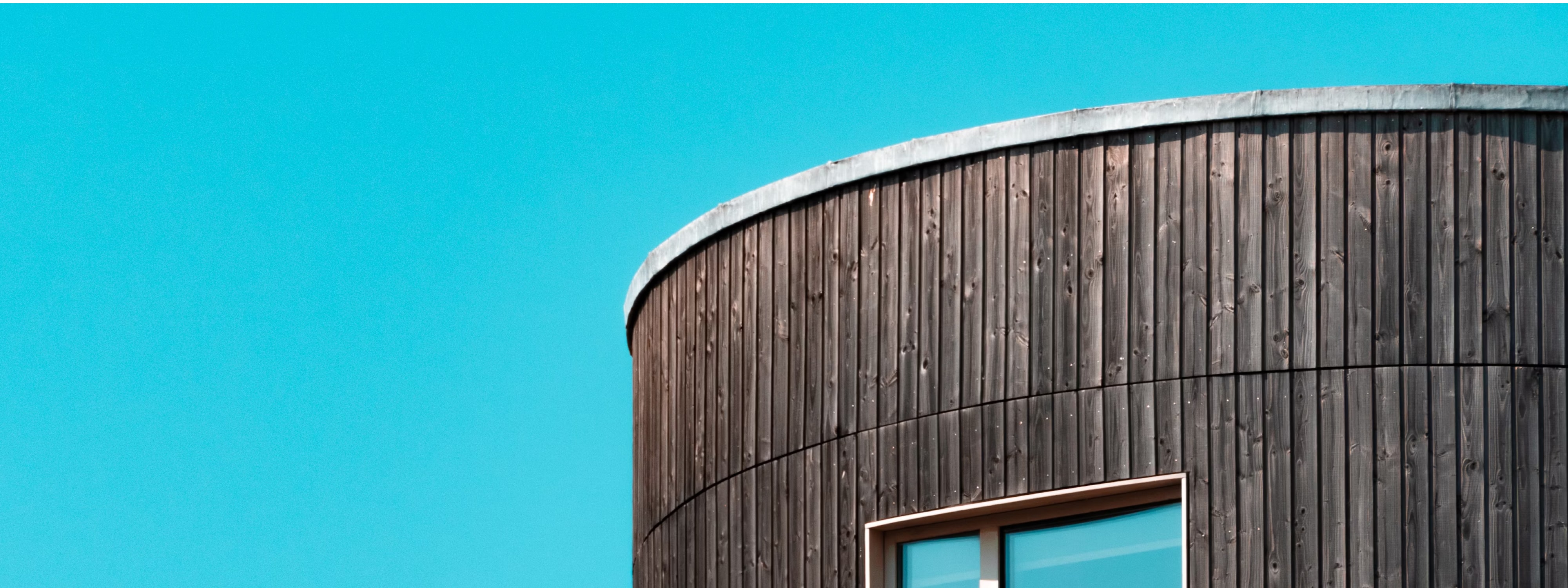Curved wooden building exterior with window against bright blue sky