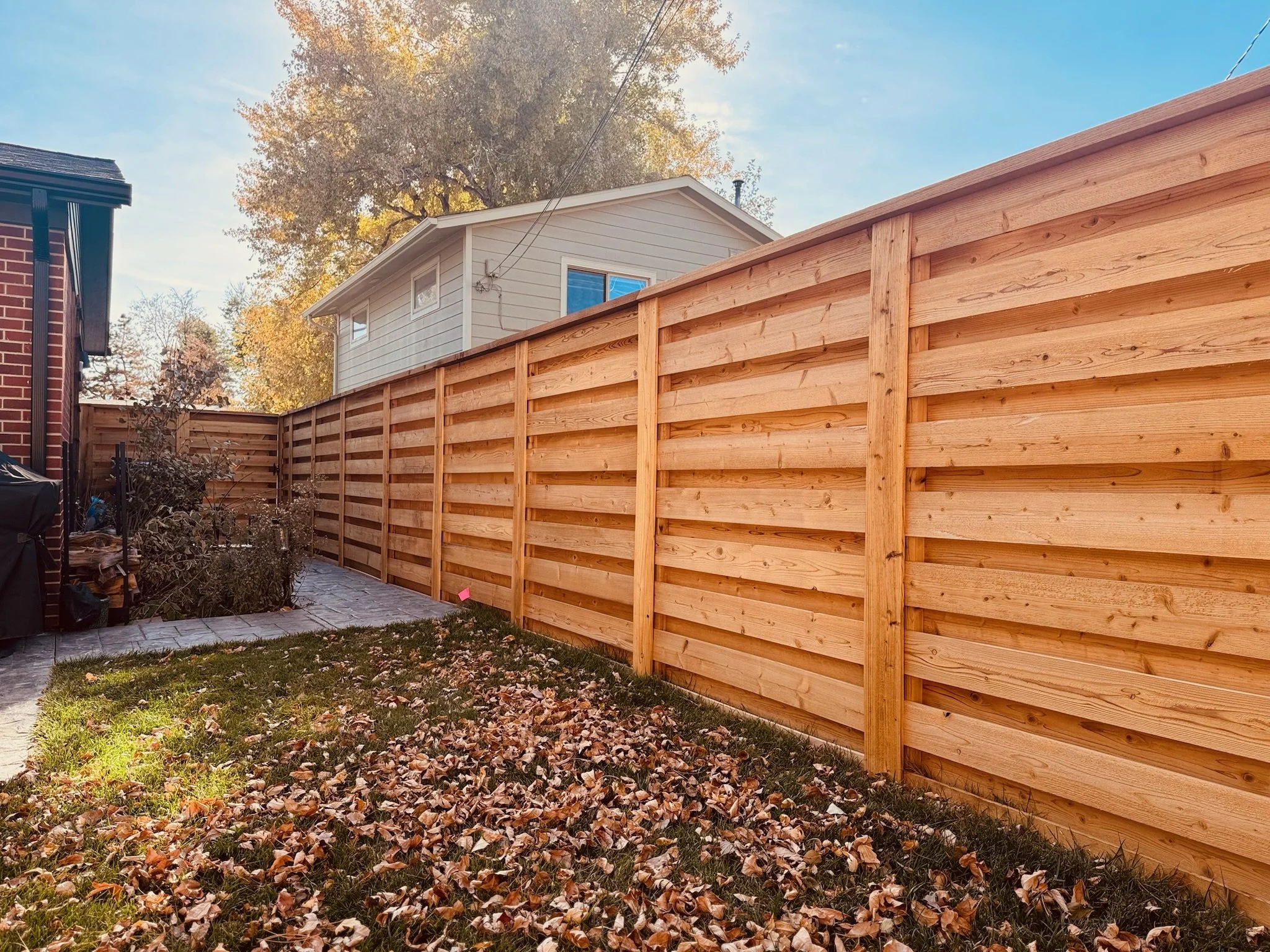 Wooden horizontal fence with fallen autumn leaves in backyard