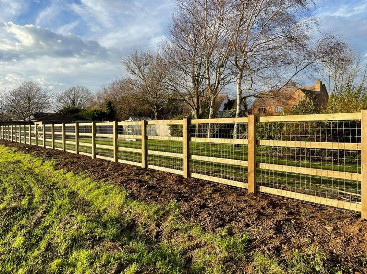 Wooden fence with wire mesh along muddy field, bare trees in background